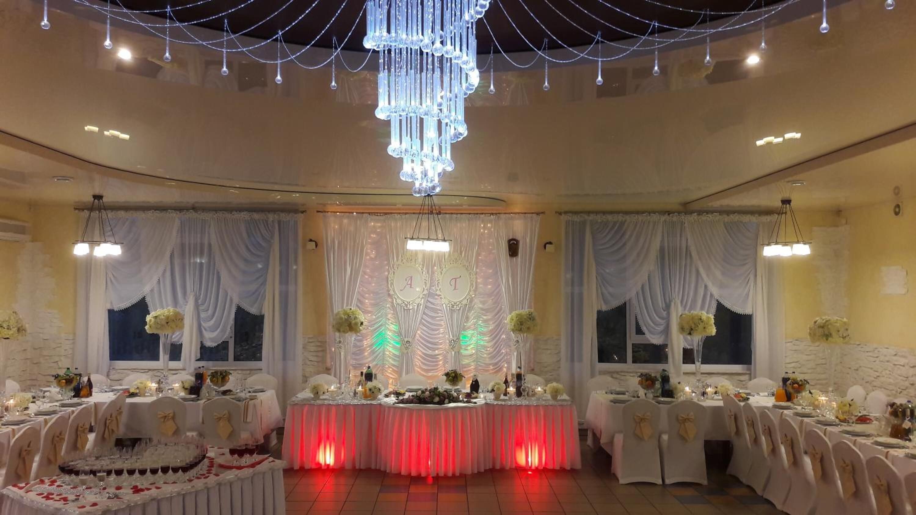 A banquet hall with round tables, white drapes, and a chandelier.
