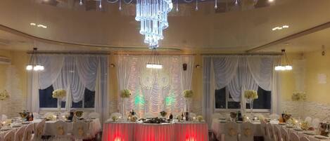 A banquet hall with round tables, white drapes, and a chandelier.