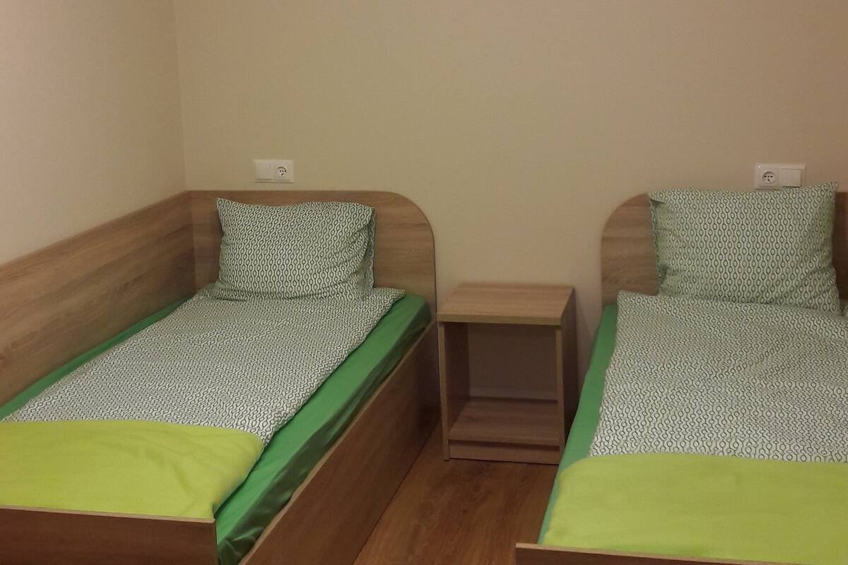 Une chambre avec deux lits en bois, une petite table de chevet et un ventilateur de plafond.
