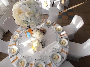 A round dining table set for a meal with white chairs, plates of food, and clear glassware. - Restauracja i Sala Bankietowa AS - Noclegi (Turek)