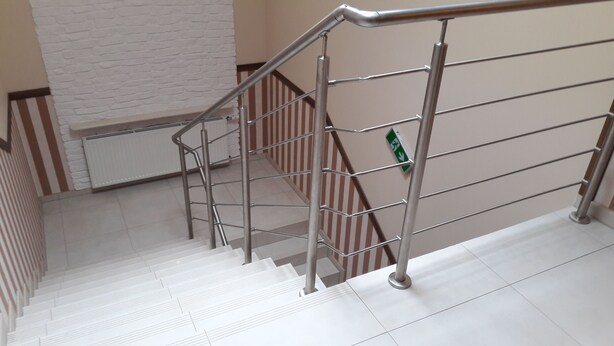 Un escalier avec des rampes en métal et un mur blanc orné d’un motif texturé.