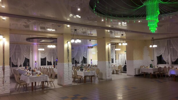 Une salle de banquet spacieuse, dotée de nombreuses tables rondes, de tentures blanches et de luminaires verts suspendus.