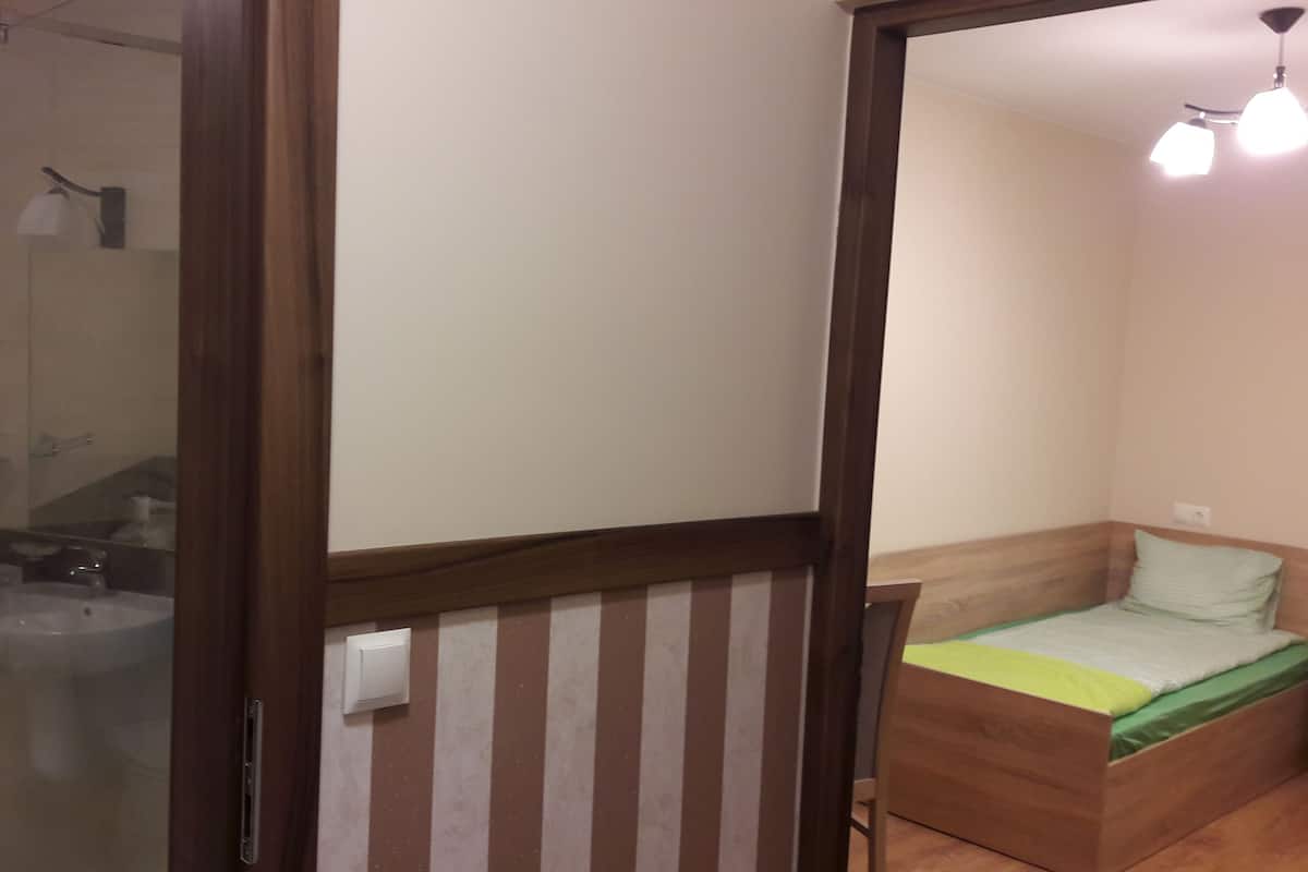 Une petite pièce, de taille modeste, comprenant un lit en bois, une table de chevet, un miroir et un espace douche.