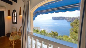 Una habitación con vista al mar, un balcón con barandilla blanca y una ventana con toldo azul.