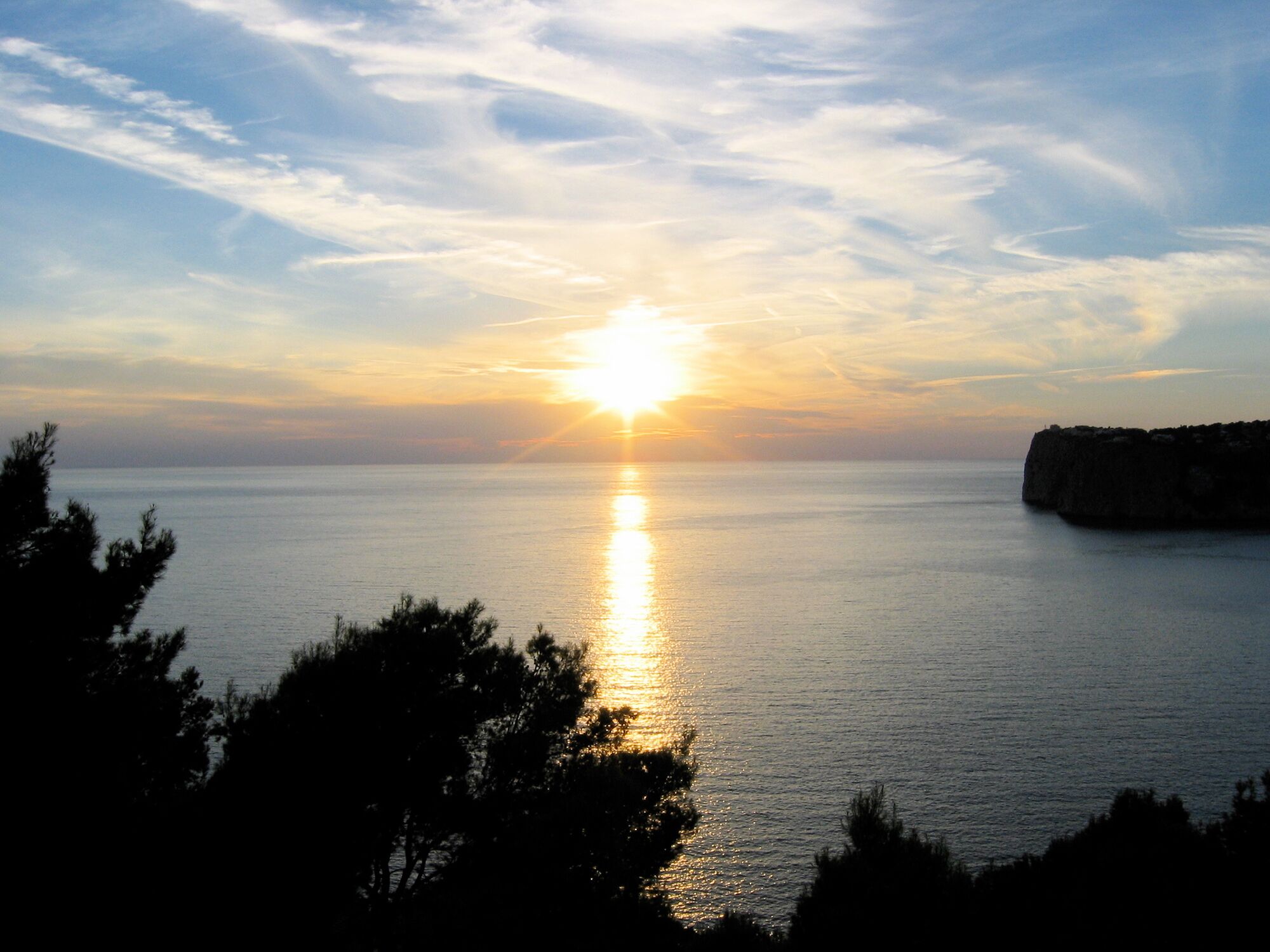 Un atardecer sobre un mar tranquilo con un promontorio rocoso a la derecha.