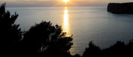 A sunset over a calm sea with a rocky outcrop on the right.