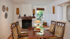 Un comedor con una mesa de madera, cuatro sillas, una chimenea y platos decorativos en la pared.