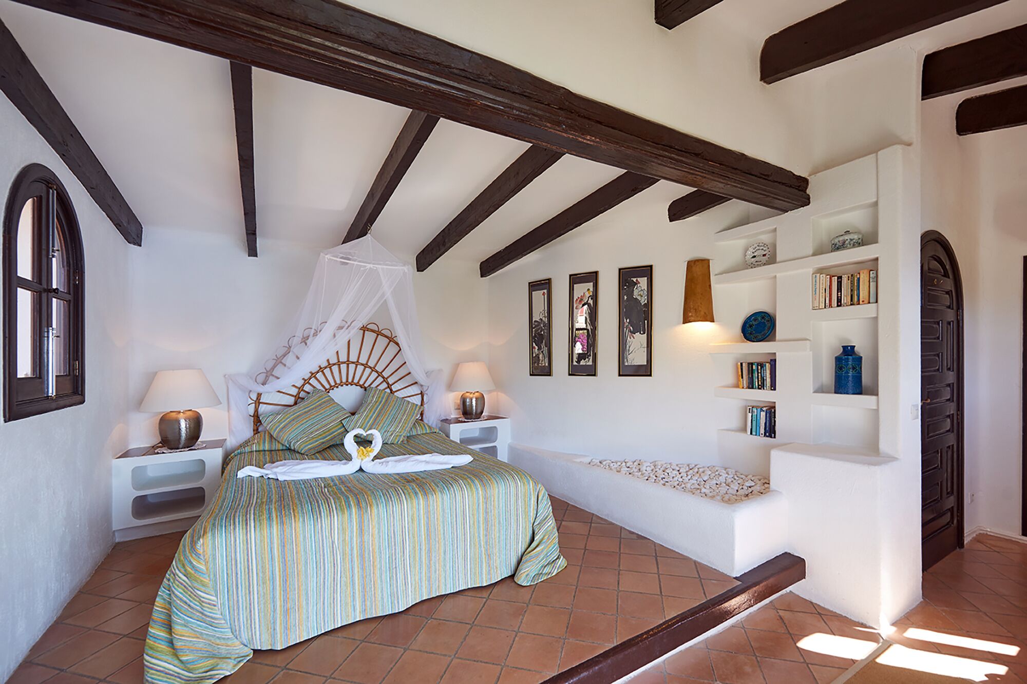 A bedroom with a bed, bedside lamps, a bookshelf, and a window.