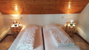 Een kamer met twee eenpersoonsbedden, elk voorzien van een kussen en een dekbed, aan weerszijden van houten nachtkastjes met lampen.