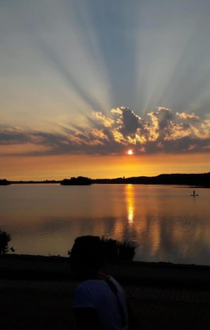 Un atardecer sobre un lago tranquilo con la silueta de una persona al frente.
