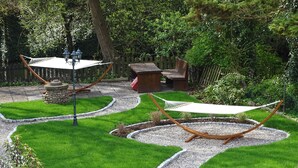 Ein gepflegter Garten mit einer Hängematte, einer Steinhlaterne und einem Holztisch.