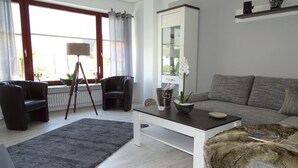 Ein modernes Wohnzimmer mit einem grauen Sofa, einem schwarzen Ledersessel, einem Couchtisch und einem schwarzen Teppich.