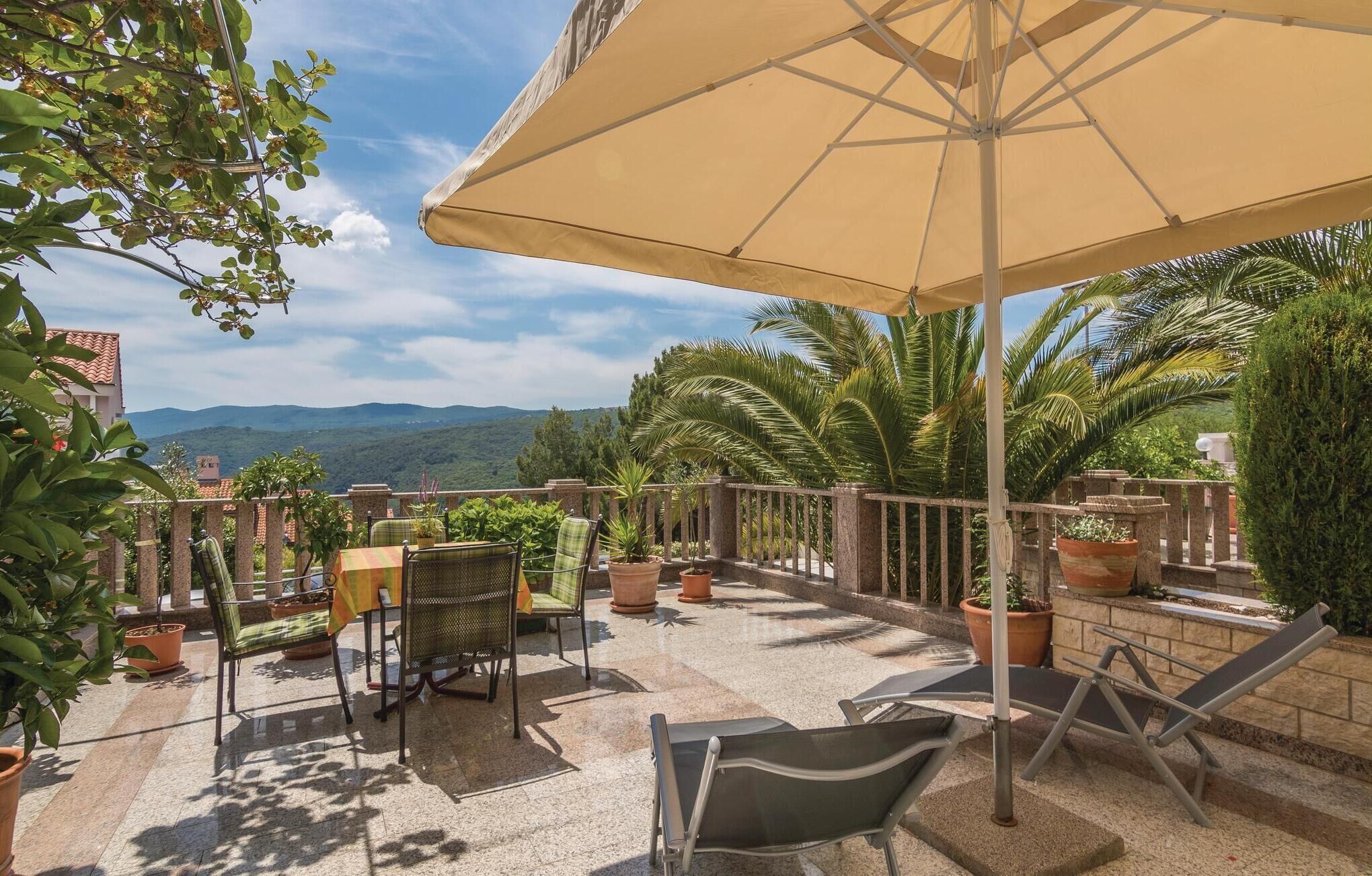 A terrace with a table and chairs, a large umbrella, and potted plants.