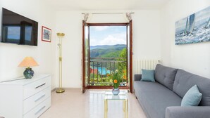 A living room with a sofa, a TV, a lamp, a glass coffee table with flowers, and a balcony with a view of the sea and hills. - Lovely apartment in Rabac with WiFi (Rabac)