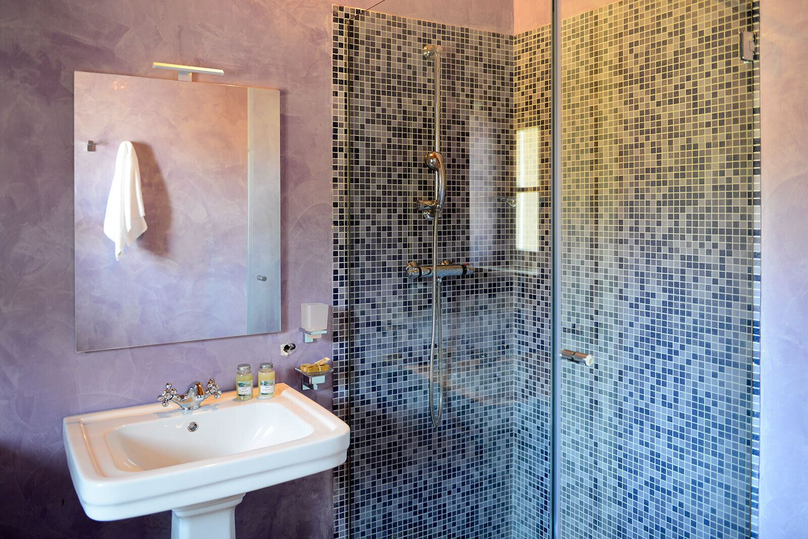 Een badkamer met een witte wastafel, een spiegel en een douche met mozaïektegels.