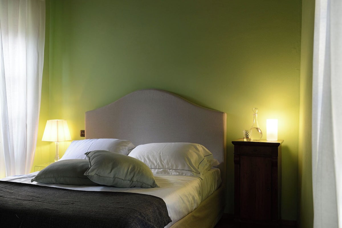 Una cama bien hecha con almohadas, una lámpara de noche y una mesita de noche con lámpara.