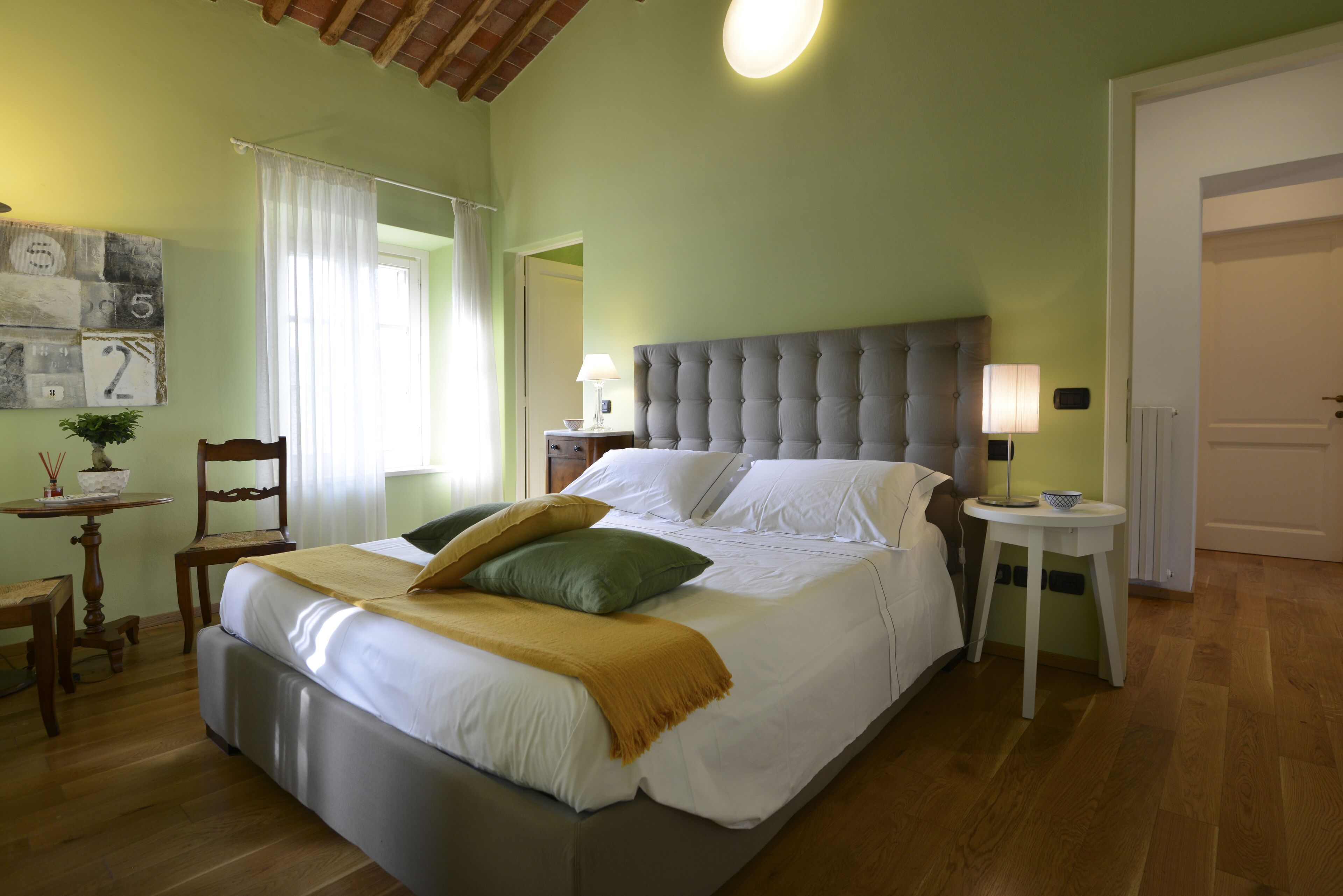 A neatly arranged bedroom with a large bed, a bedside table, a chair, and a small table with a lamp.