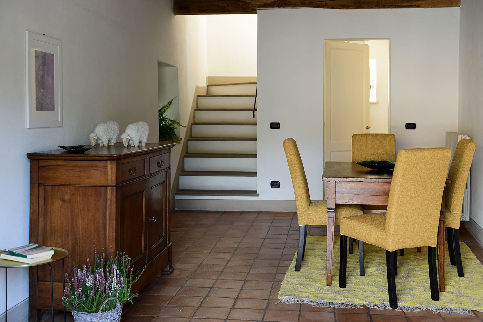 A dining area with a table and chairs, a wooden cabinet, and a staircase in the background.