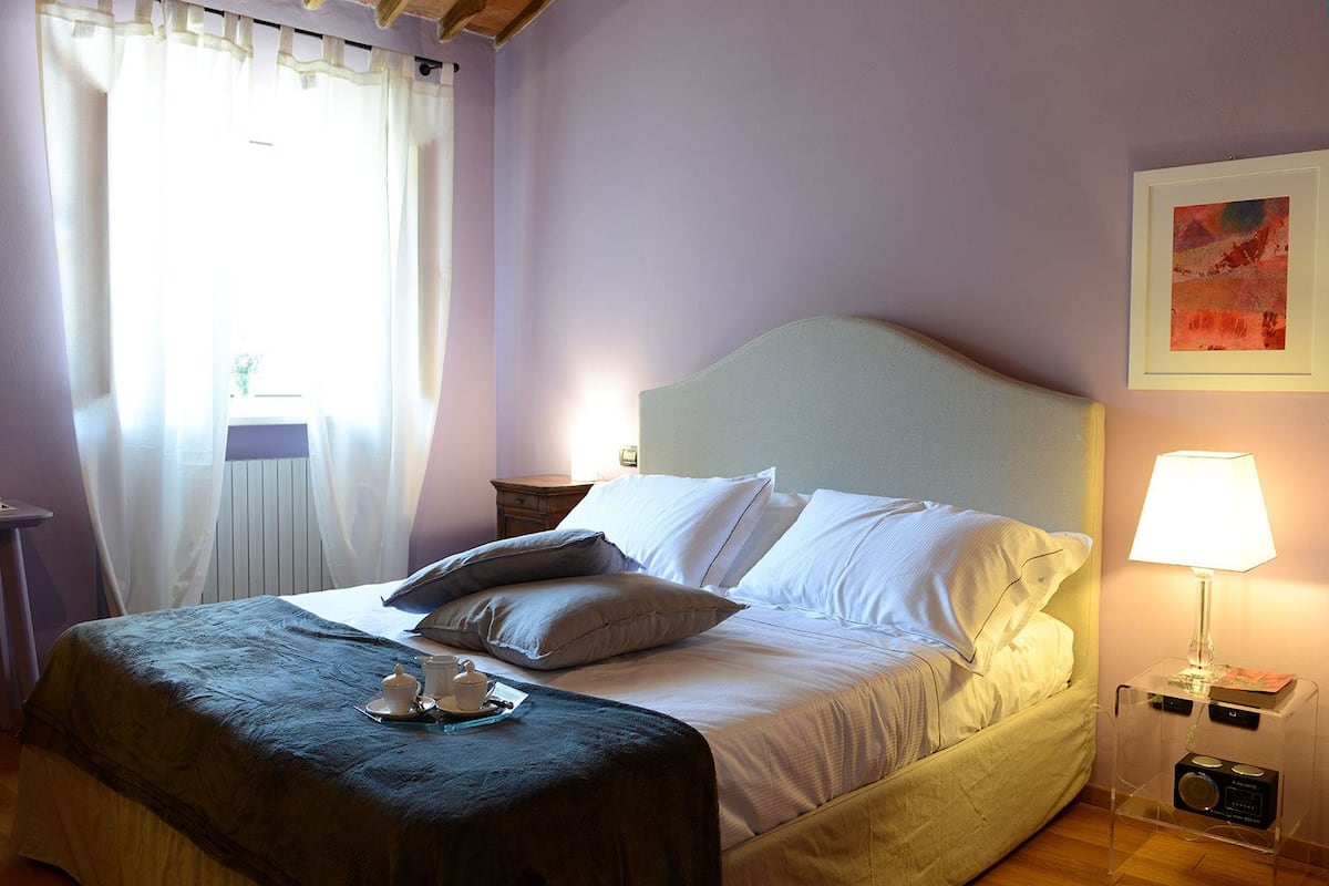 Una cama bien hecha con almohadas, una mesita de noche con lámpara y una ventana con cortinas.