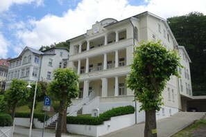 Um edifício de vários andares com estilo arquitetônico clássico, apresentando uma escadaria central e uma varanda no segundo andar.