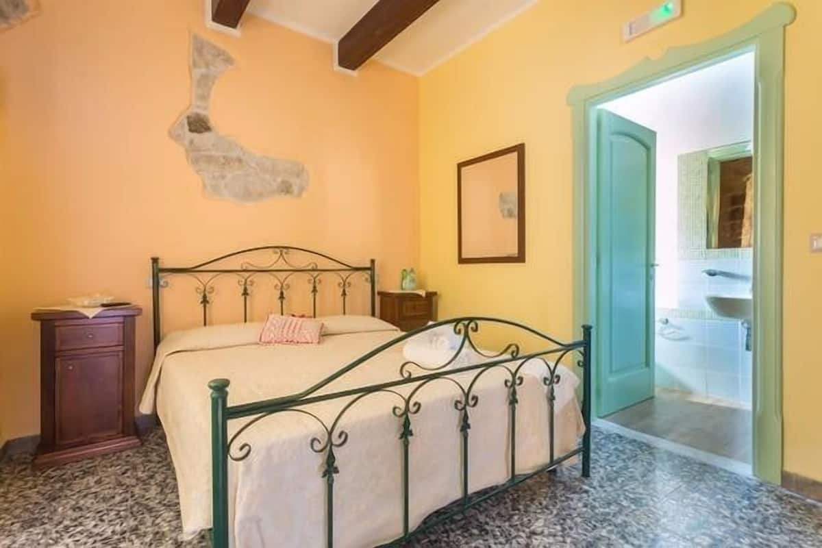 Une chambre à coucher comprenant un lit, une table de chevet, une étagère fixée au mur et une porte donnant accès à une salle de bain.