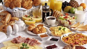 Un assortiment de produits pour le petit-déjeuner comprenant des croissants, des viennoiseries, du fromage, du jambon, des œufs, ainsi que divers fruits et boissons.