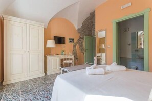 Un dormitorio con cama, escritorio, silla, armario y baño visible a través de una puerta abierta.