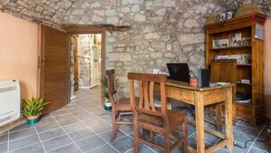 Une pièce rustique avec un mur en pierre, un bureau en bois sur lequel se trouve un ordinateur portable, une bibliothèque et une porte donnant sur une autre pièce.