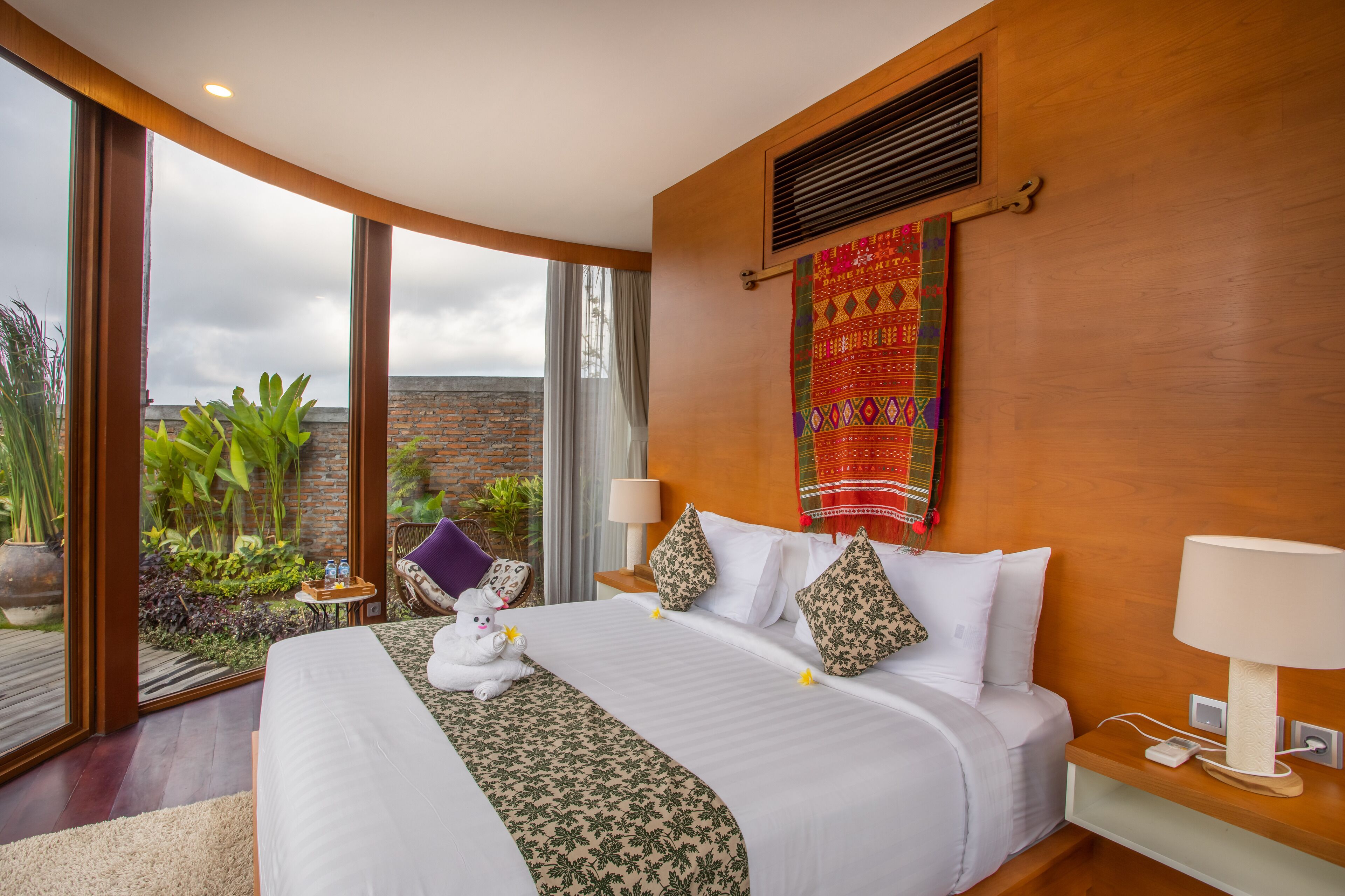 A spacious bedroom with a large bed, a nightstand, a lamp, and a view of the outdoors.