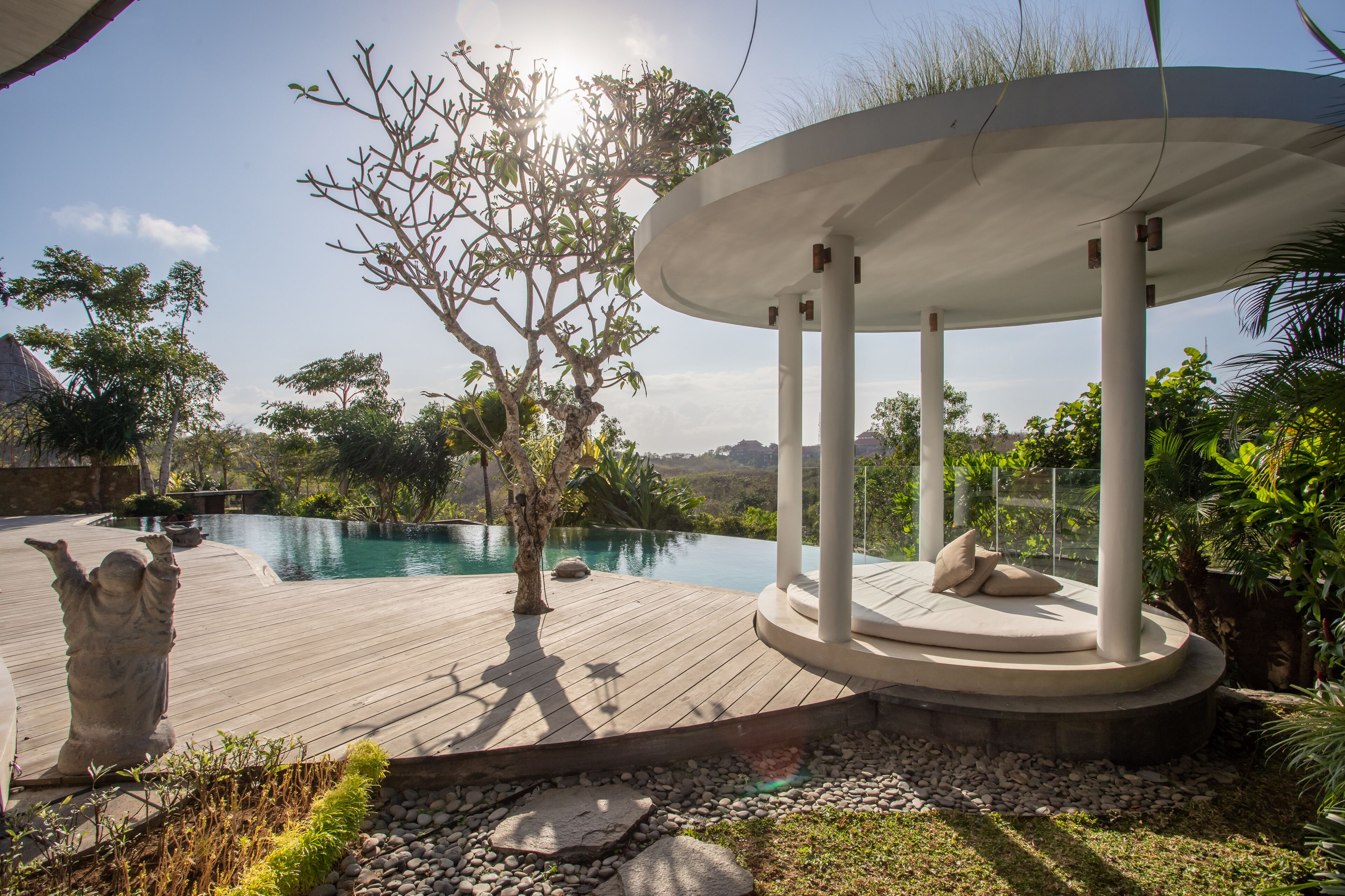 A wooden deck with a circular seating area, a statue, and a pool.