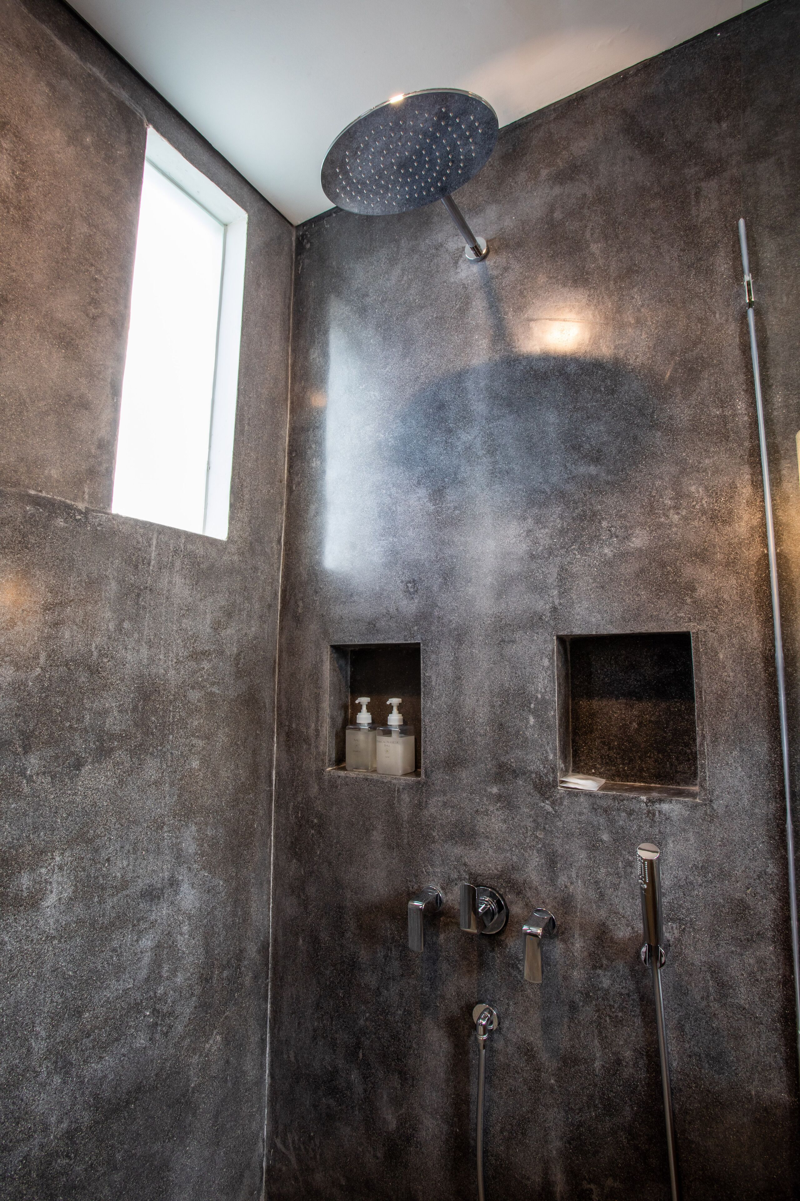 A modern bathroom with a large shower, a window, and built-in soap dispensers.