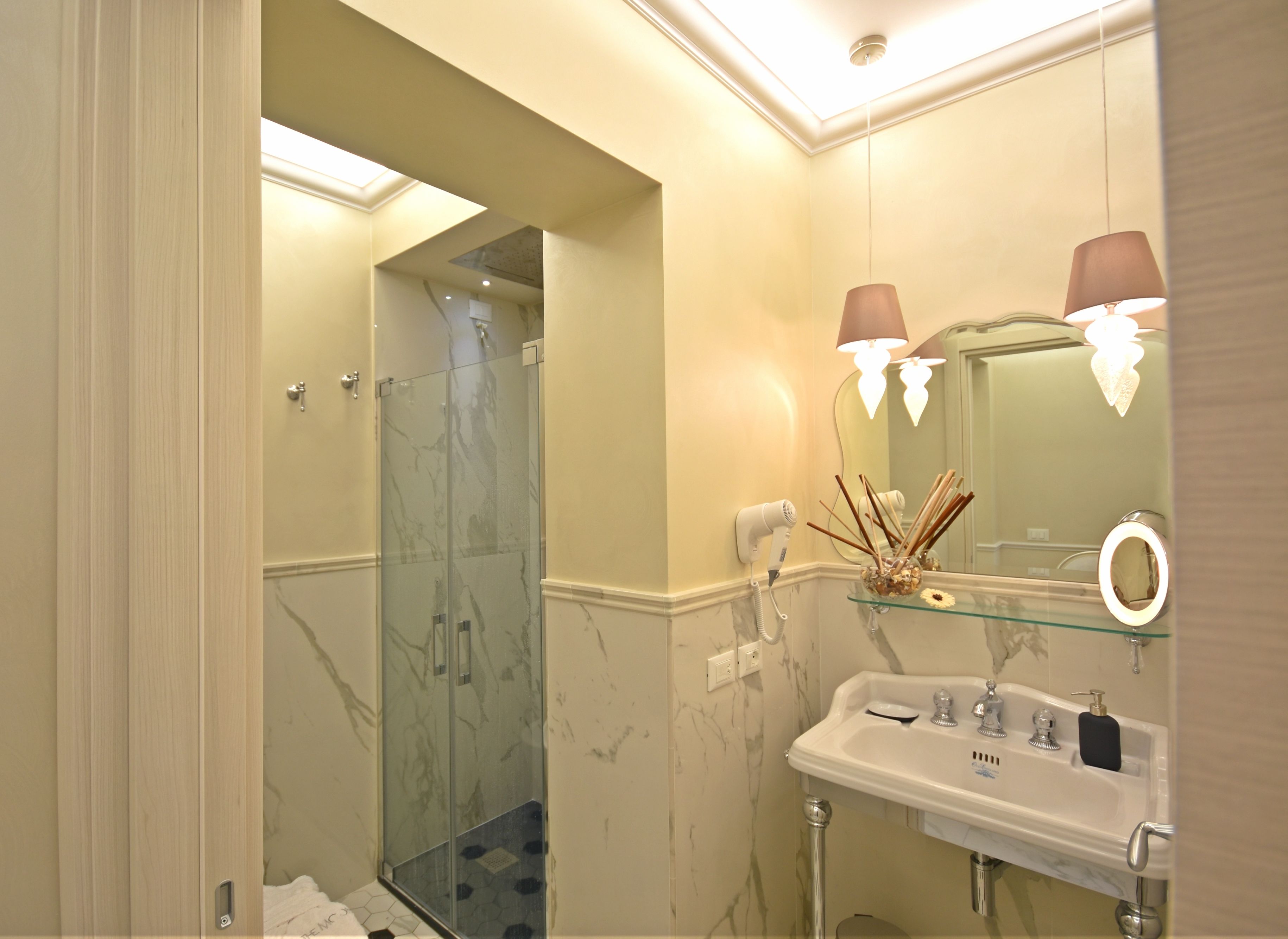 A bathroom with a glass shower, a sink with a mirror, and two wall-mounted lamps.