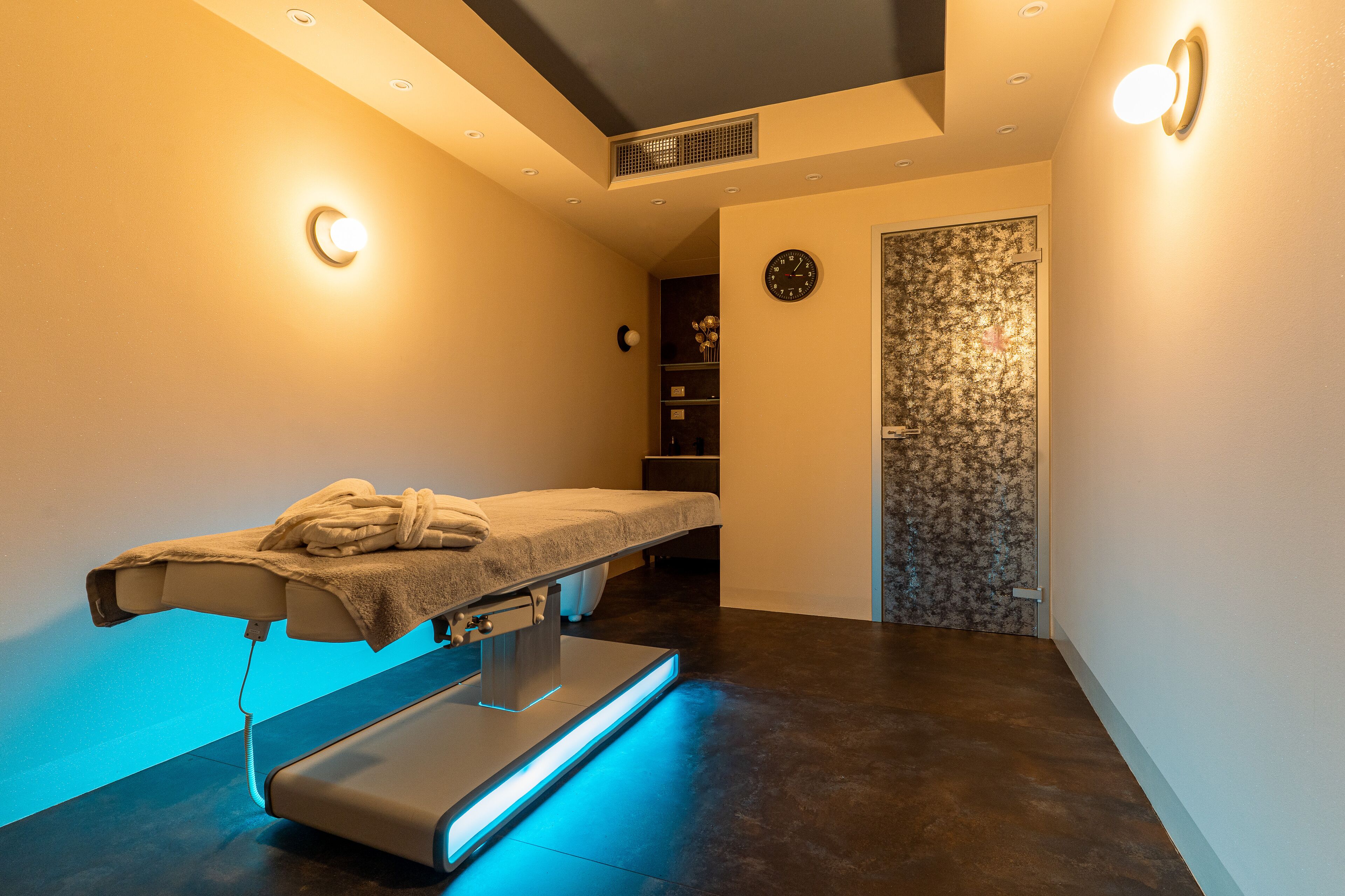 A massage therapy room with a massage table, a towel, and a clock on the wall.