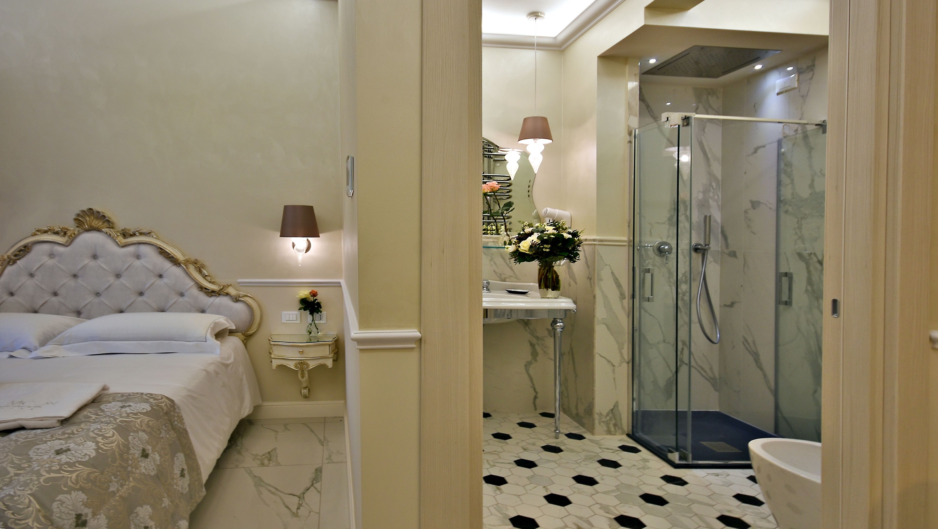 A bedroom with a large bed, a bedside table with a lamp, and a bathroom with a shower, toilet, and sink.