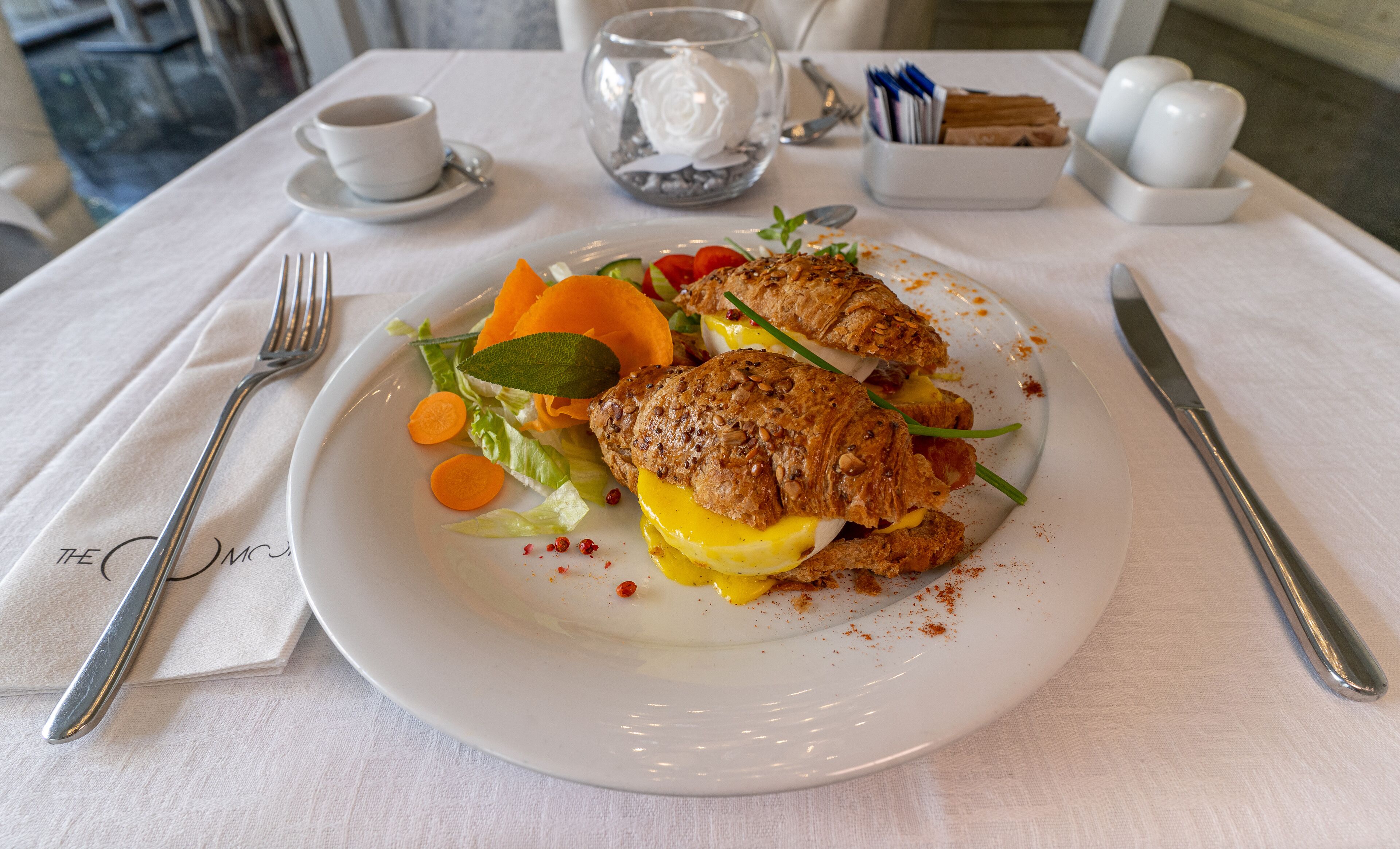 Un plato de comida con un sándwich y verduras sobre un mantel blanco.