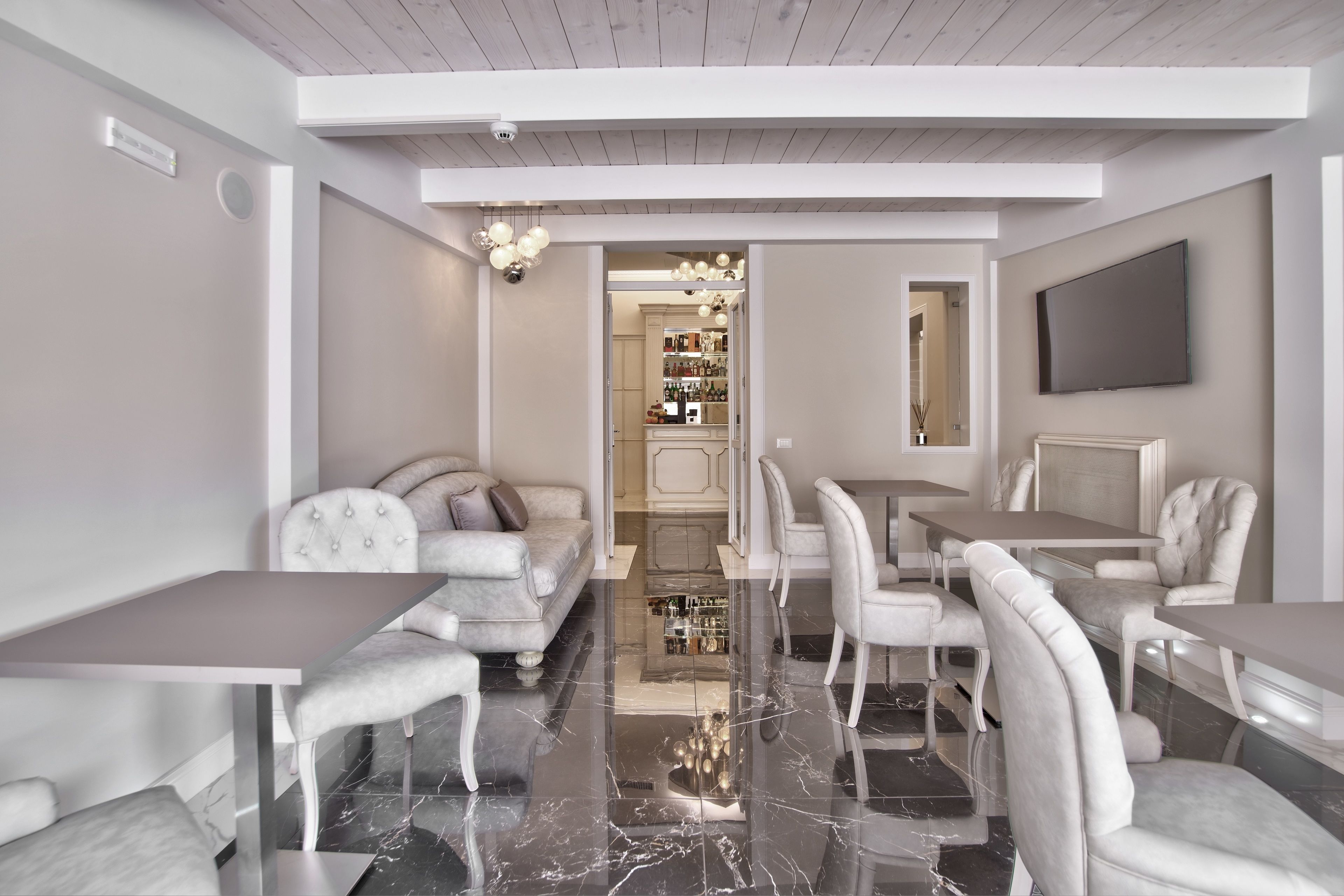 Un comedor moderno con suelo de mármol, mobiliario blanco y una araña.