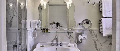 A modern bathroom with a large mirror, two wall-mounted lights, a glass-enclosed shower, a white sink with chrome fixtures, and a towel rack with white towels.