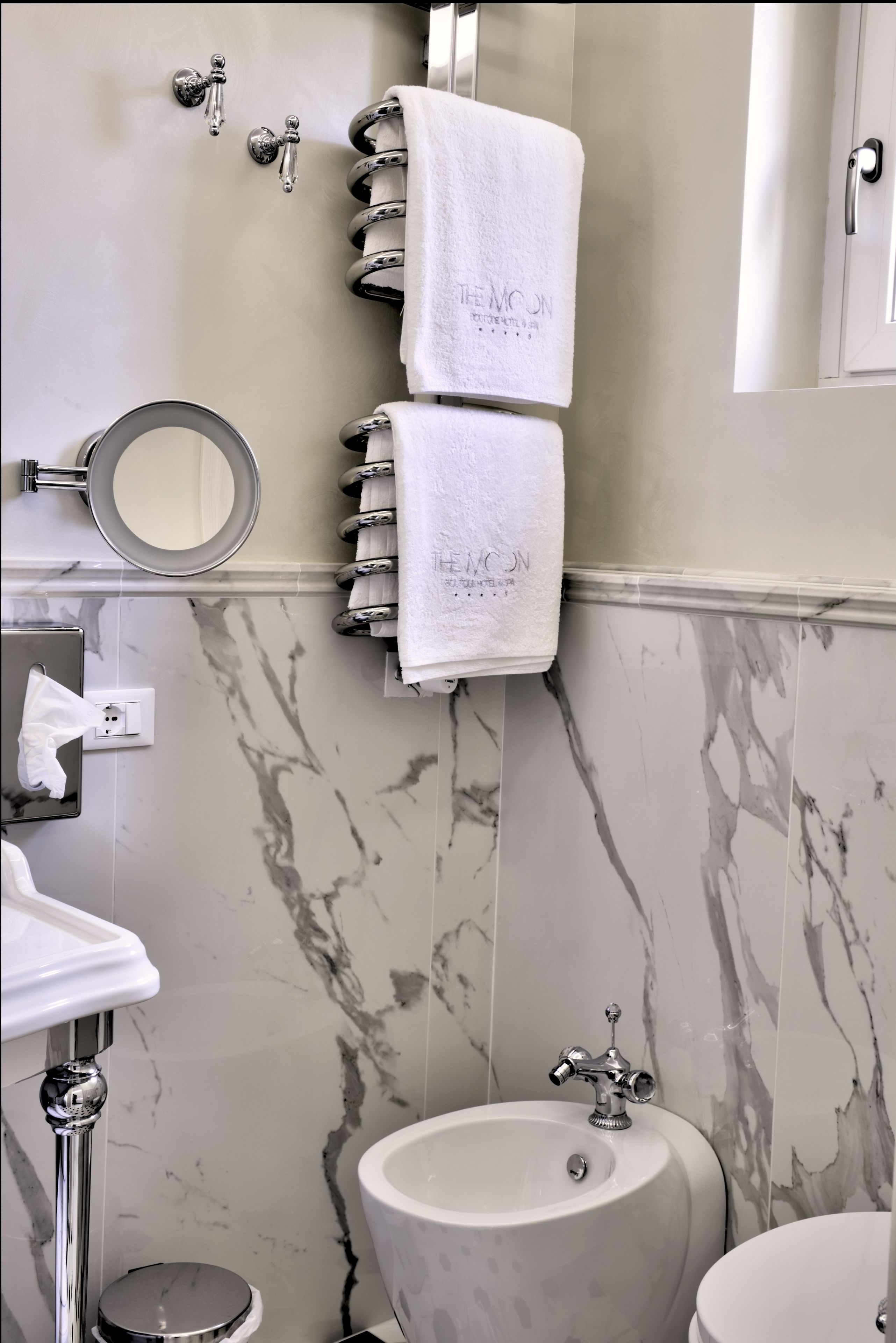 A bathroom with marble walls, a sink, a bidet, and a towel rack with two towels.
