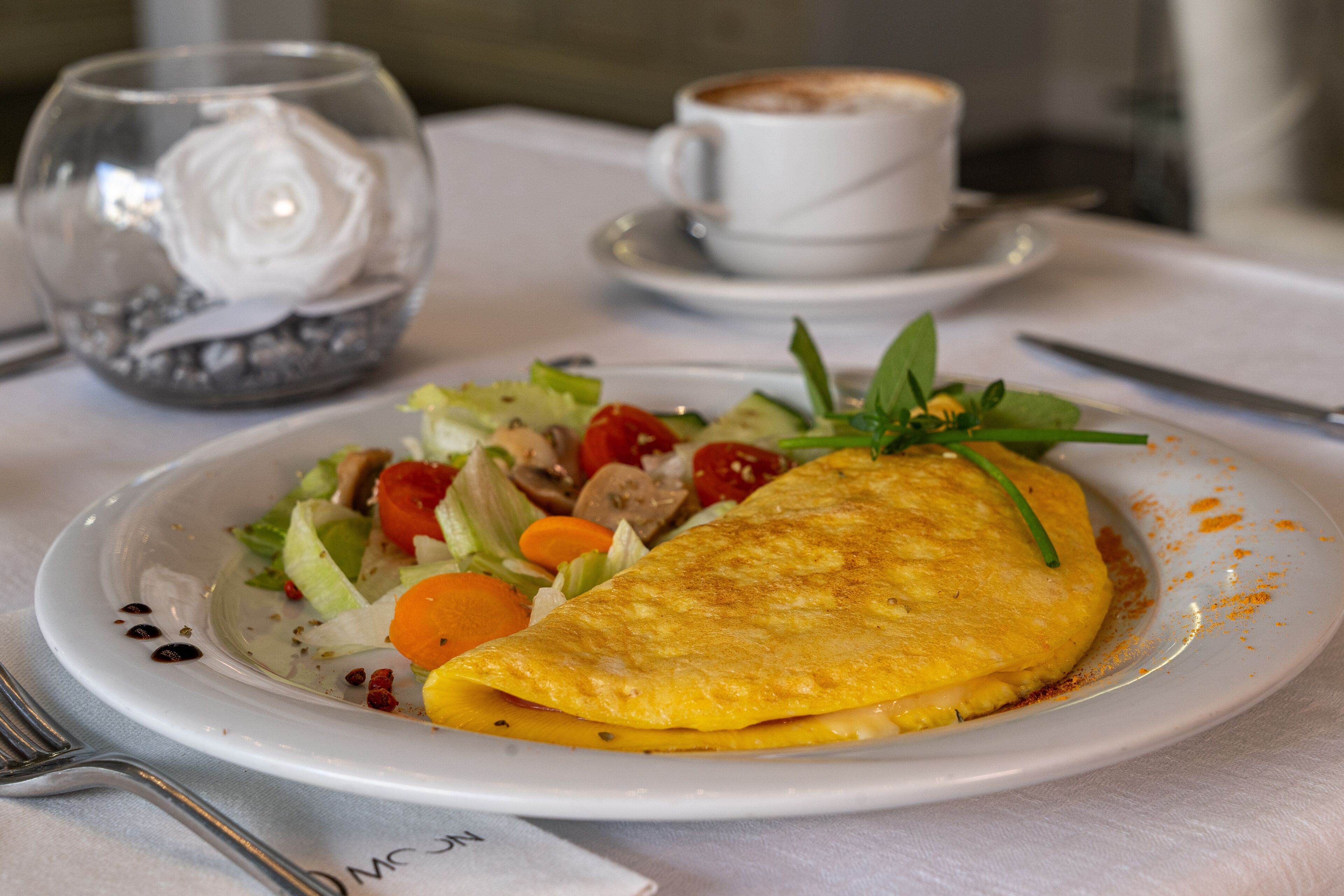 Une assiette contenant une omelette, une salade et une tasse de café, posée sur une table.