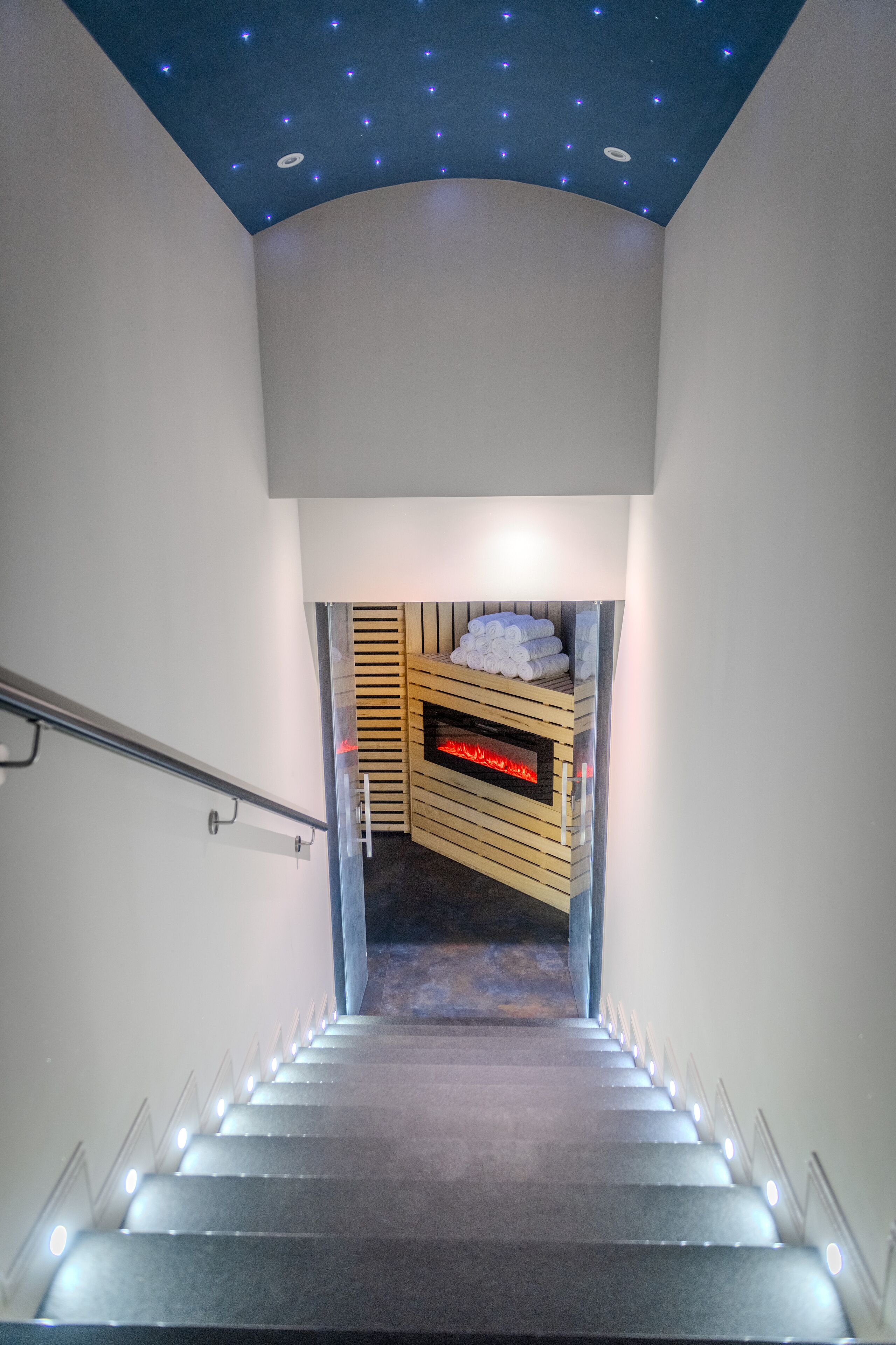 Una escalera que conduce a una habitación con sauna y toallas, bajo un techo decorado con un diseño de estrellas.