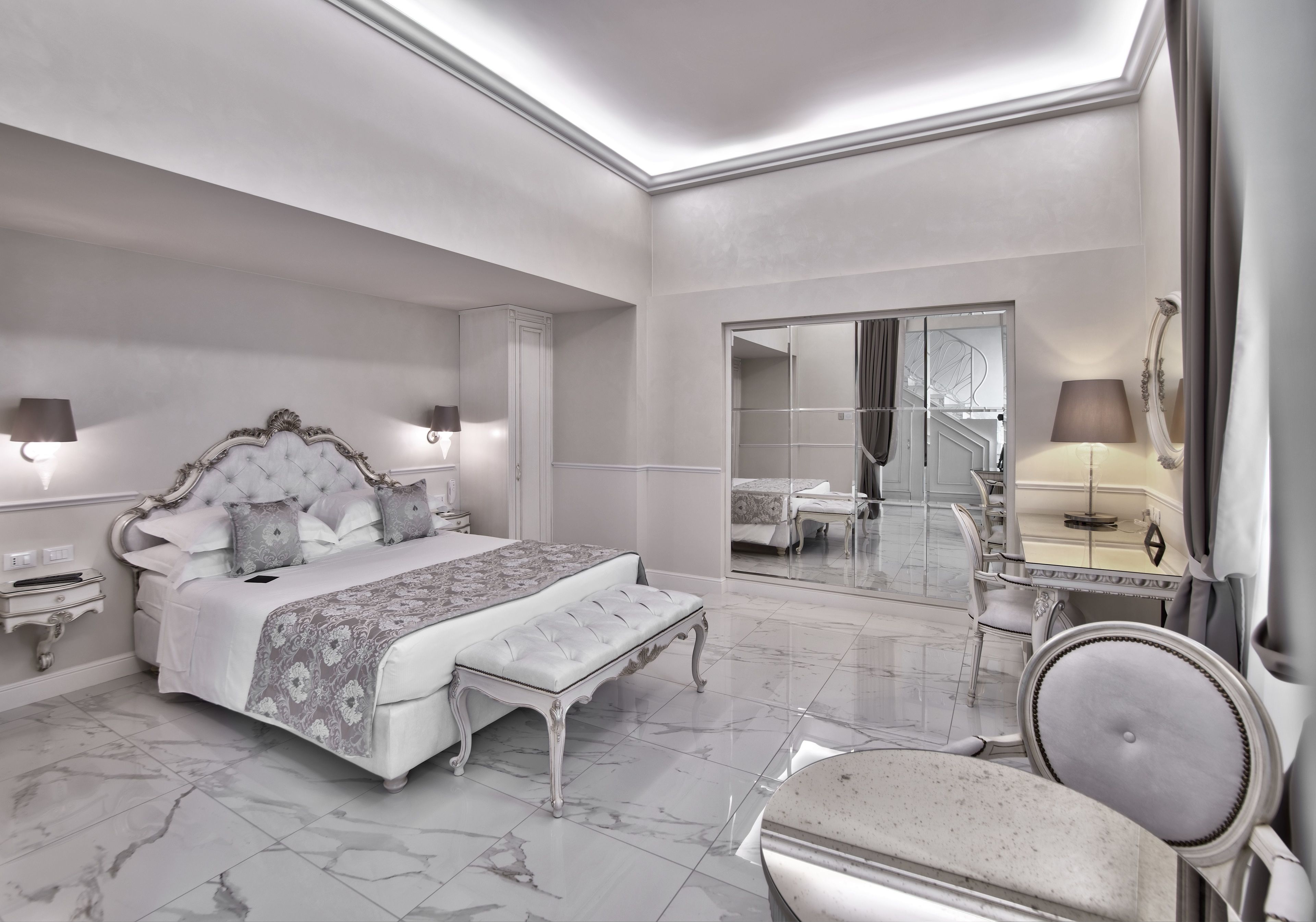 A spacious bedroom with a large bed, a sitting area, a vanity with a mirror, and a walk-in closet.
