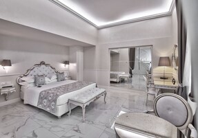 Un'ampia camera da letto con un letto grande, un angolo relax, una toeletta con specchio e un cabina armadio.