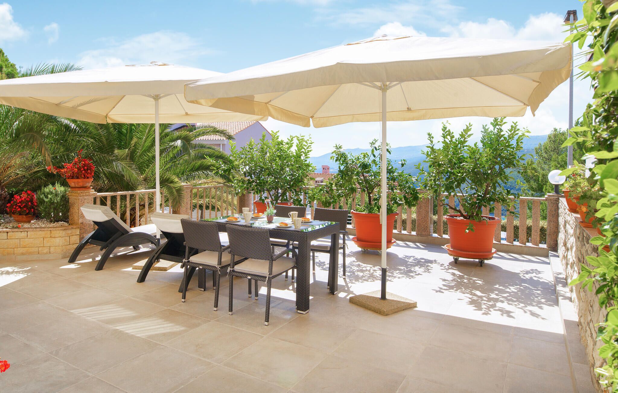 An outdoor patio with a table and chairs, surrounded by potted plants and umbrellas.