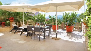 An outdoor patio with a table and chairs, surrounded by potted plants and umbrellas. - Beach front apartment in Rabac with WiFi (Rabac)