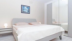A modern bedroom with a bed, bedside lamps, a framed picture, and a large mirror. - Beach front apartment in Rabac with WiFi (Rabac)