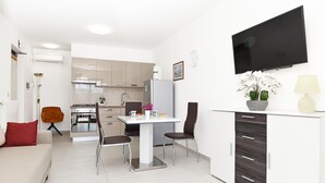 A modern kitchen with a dining area, a flat-screen TV mounted on the wall, and a sofa with a red cushion. - Beach front apartment in Rabac with WiFi (Rabac)