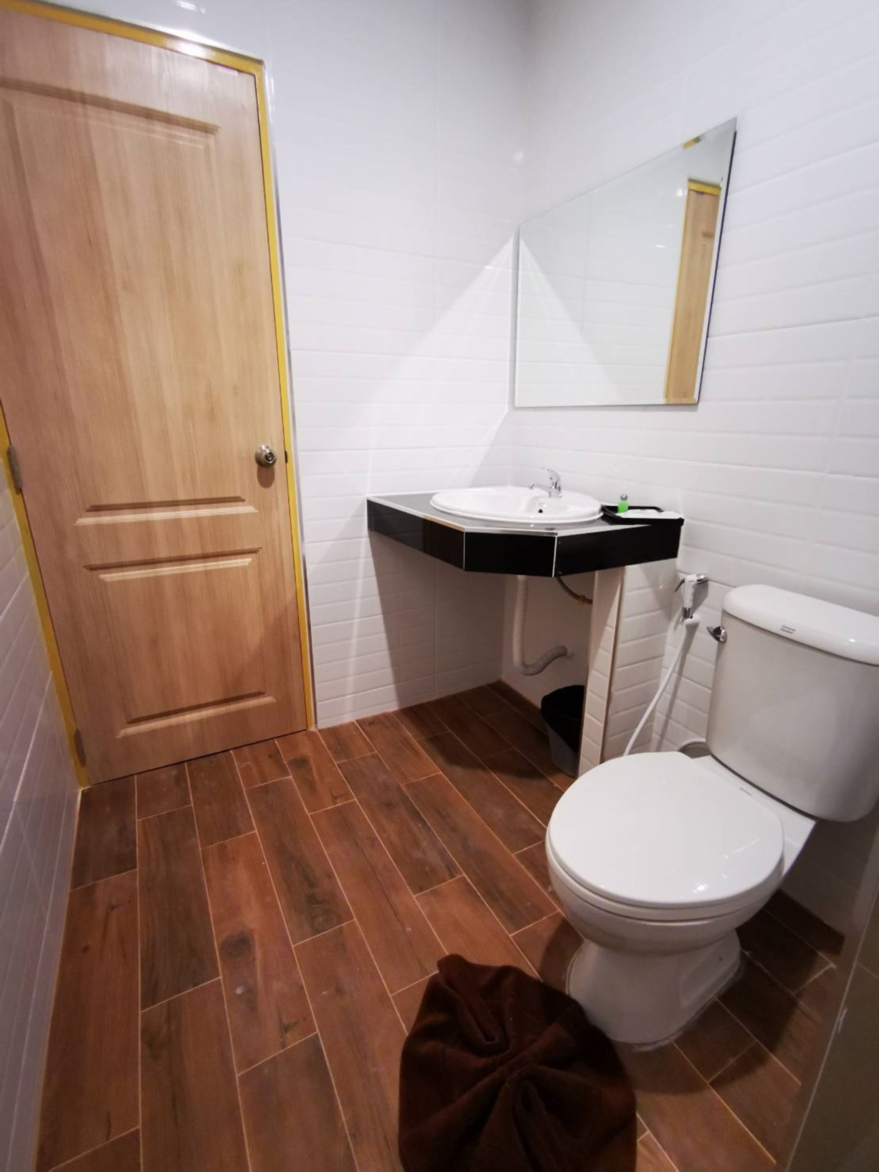 Un bagno con porta in legno, pareti piastrellate di bianco, un lavabo con piano in nero, un water bianco e uno specchio sopra il lavabo.