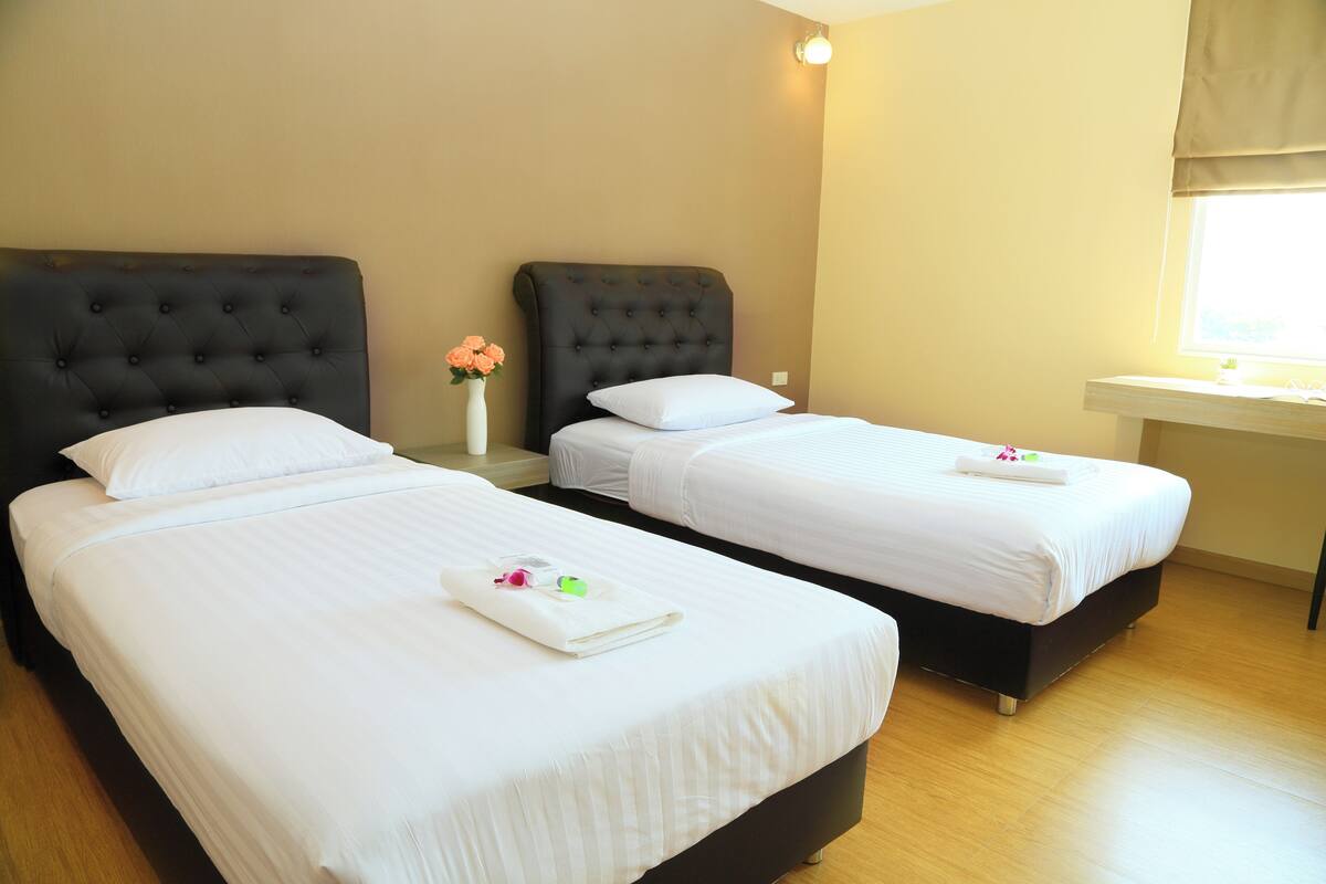 A hotel room with two beds, each with a tufted headboard, white linens, and a small vase with flowers.