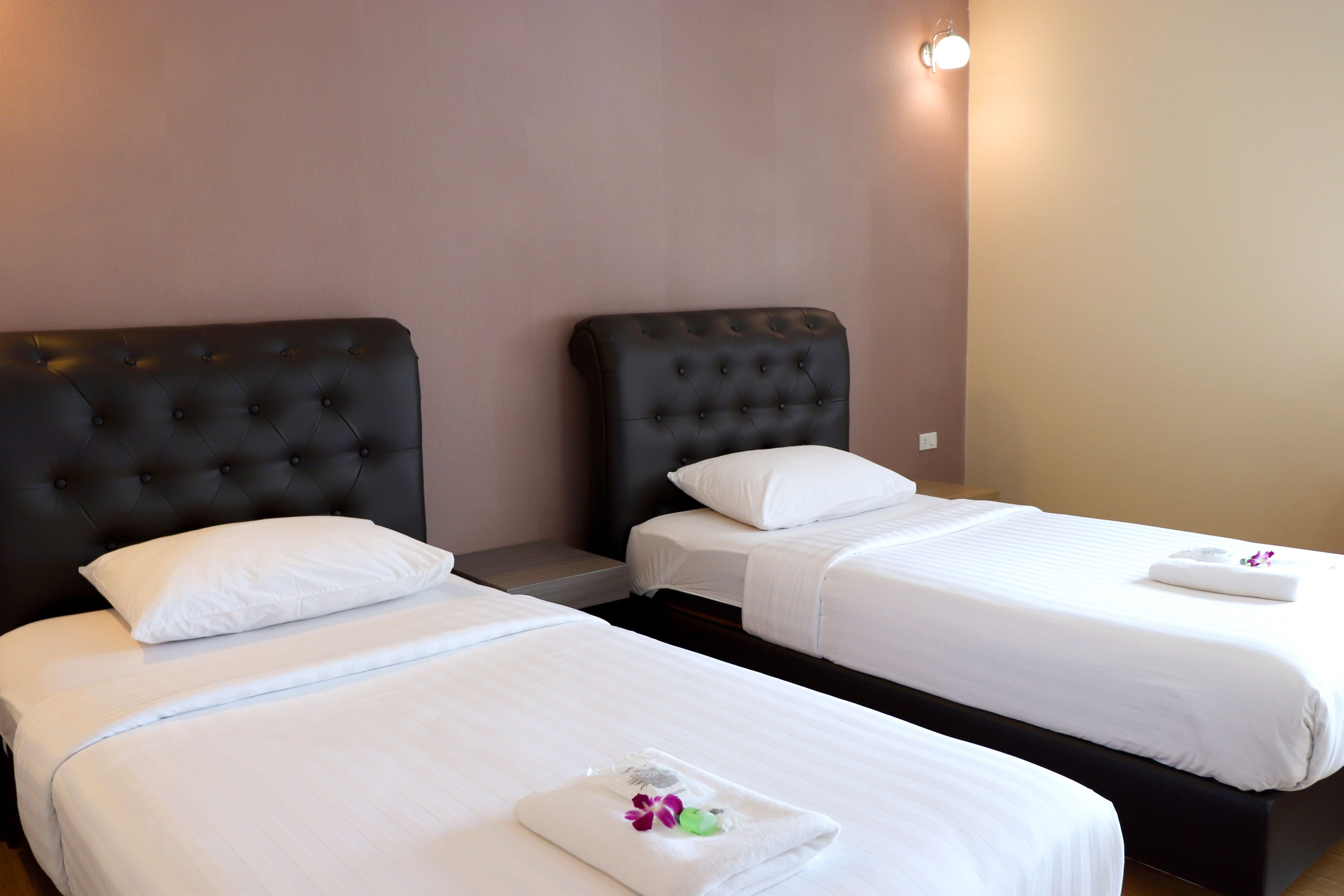Two single beds with black headboards, white linens, and a small towel with flowers on the bed.