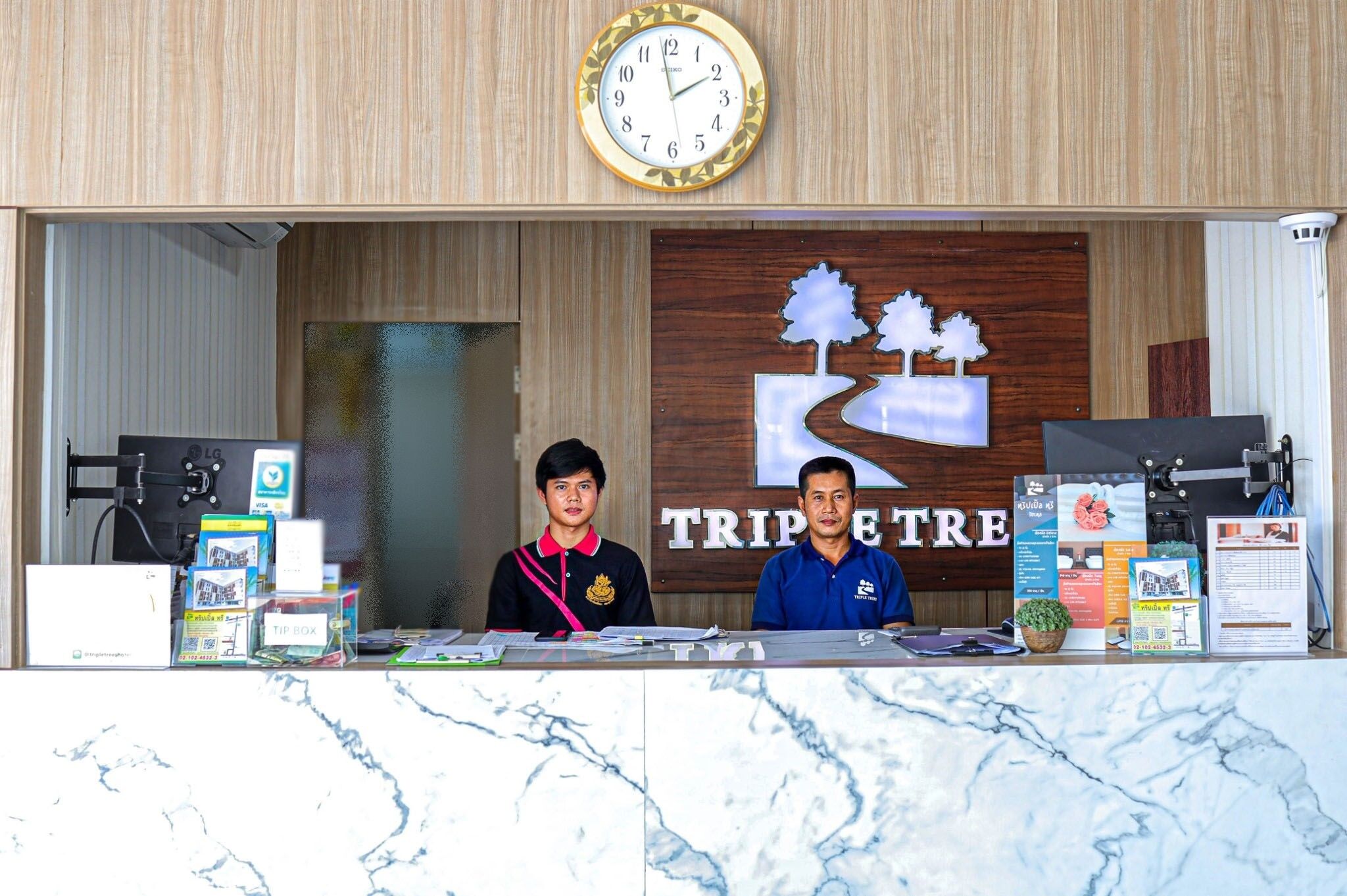 A reception desk with a clock, a wooden wall with a tree and mountain design, and various informational brochures.